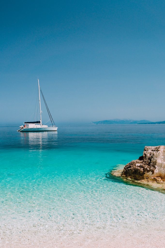 Beautiful azure blue lagoon with sailing catamaran yacht boat at anchor. Pure white pebble beach