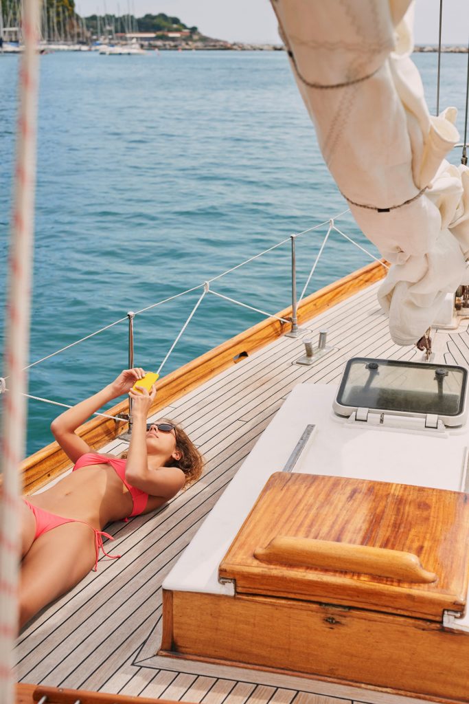 Jeune femme en bikini rouge prenant un bain de soleil sur un bateau, allongée, utilisant son smartphone pour envoyer des messages. .
